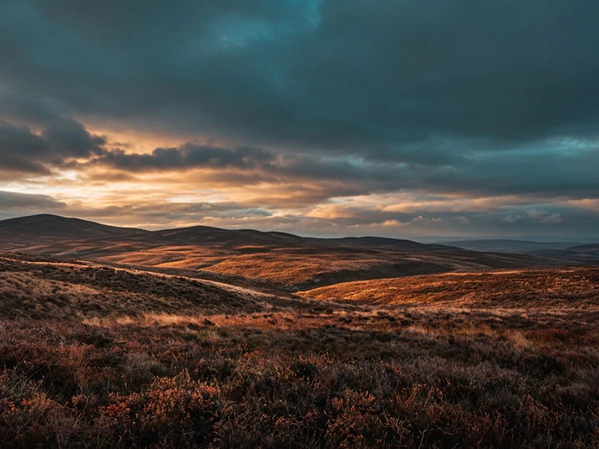 Storm clouds over open moorland breaking open to a strip of honey-gold light.